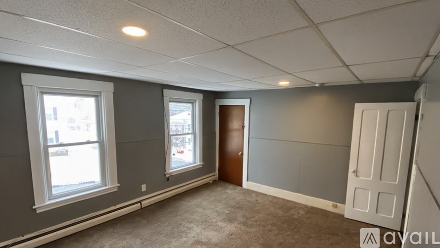 A room with a carpeted floor, two windows, and a door.