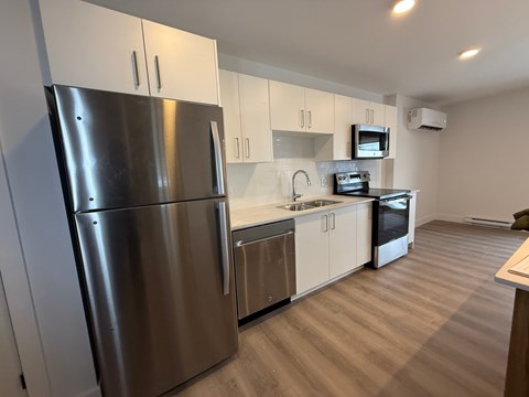 A modern kitchen with a stainless steel refrigerator and wooden flooring.