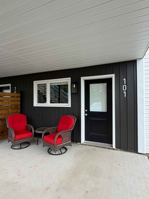 Two red chairs are on a porch.