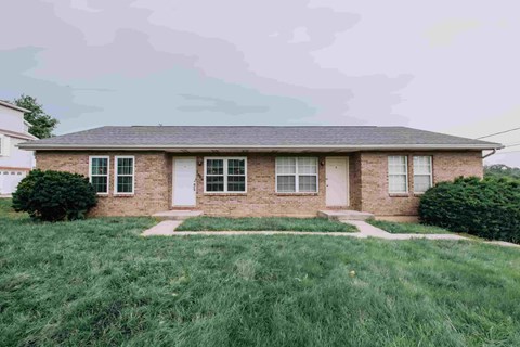 A house with a white door and windows surrounded by a green lawn.