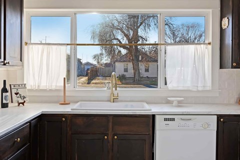 A kitchen with a white dishwasher and a window overlooking a residential area.