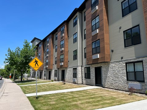 A pedestrian crossing sign is in front of a row of apartment buildings.