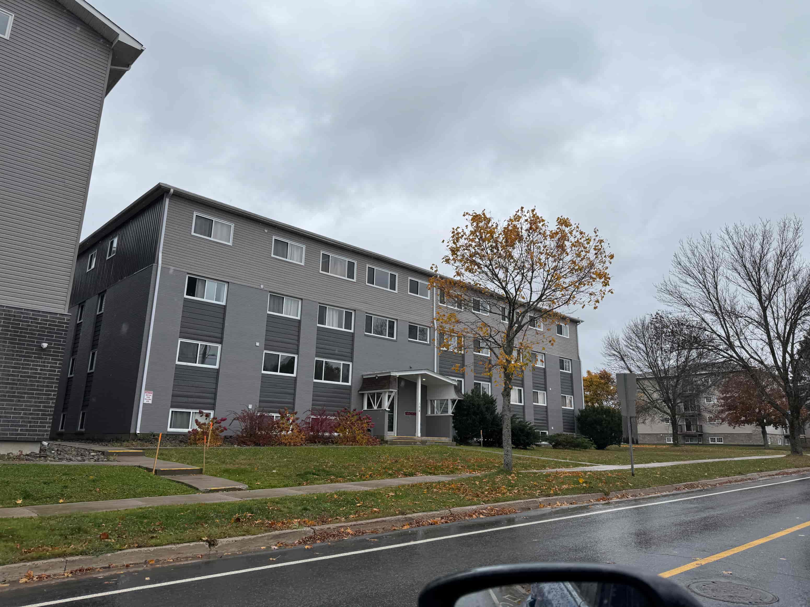 A grey apartment building with a tree in front of it.