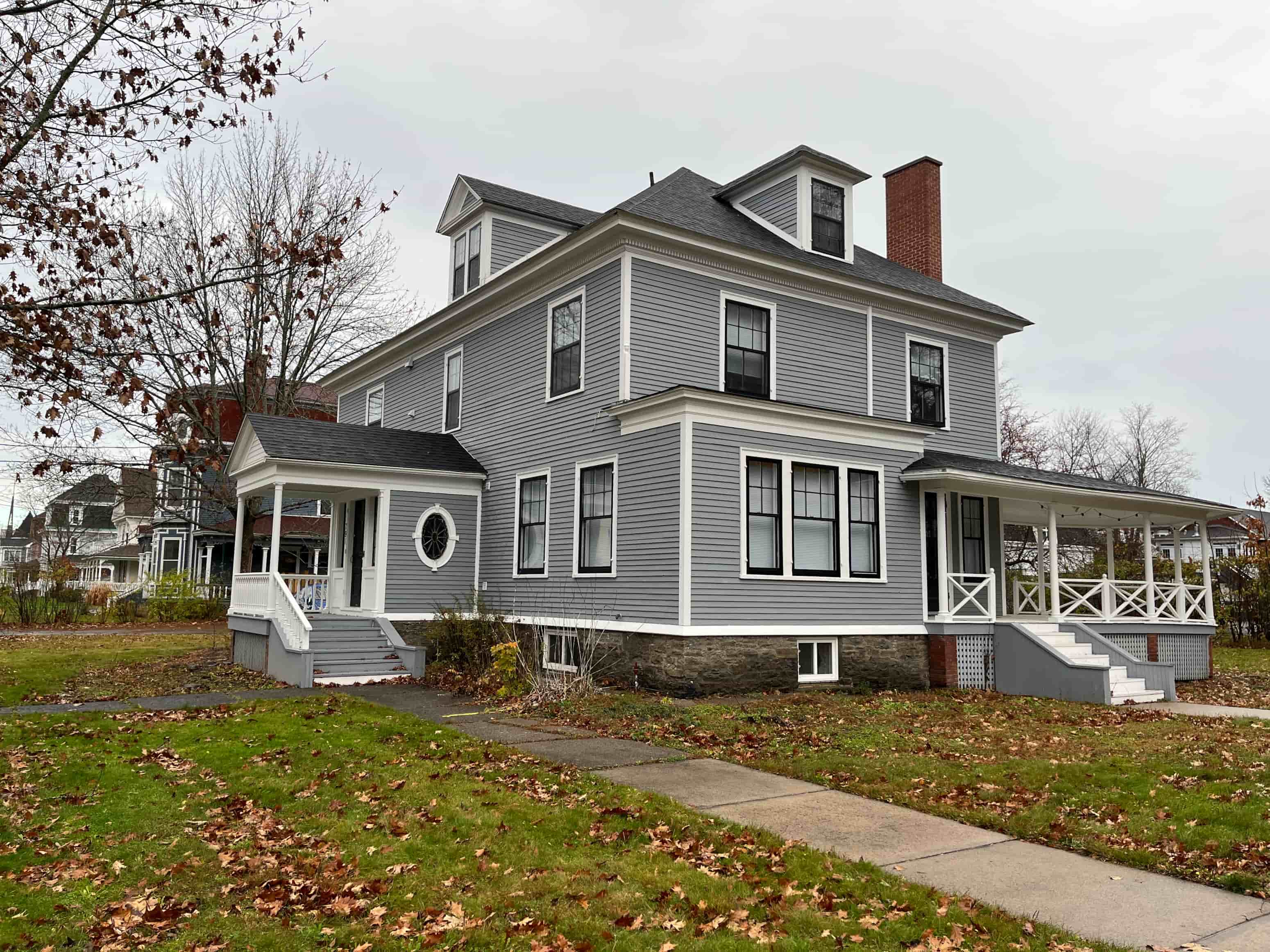 A grey house with a white porch and a brown roof.