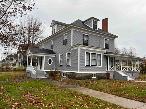 A grey house with a white porch and a brown roof.