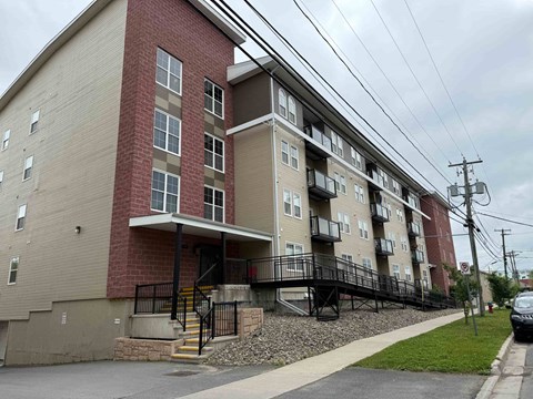 A multi-story apartment building with a red brick exterior and a balcony on the second floor.