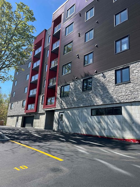 A tall building with a red and grey facade stands next to a parking lot.