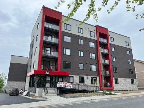 A multi-story building with a red and grey facade and a sign that says "Now Renting" and a phone number.