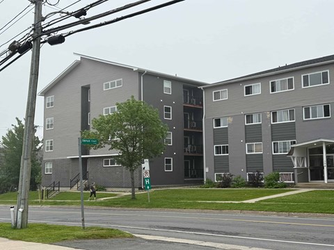 A grey apartment building with a green street sign in front.