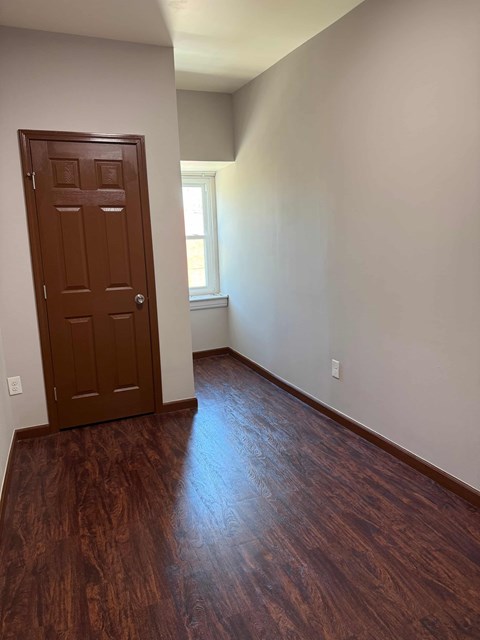 A brown door is in a room with wood flooring.