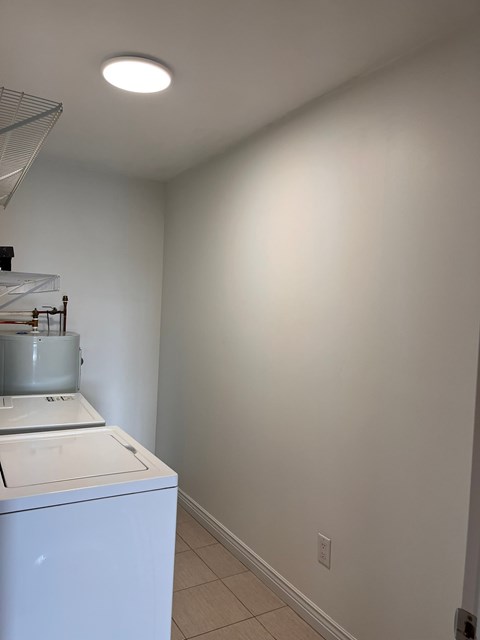 A white washing machine sits in a laundry room with white walls.