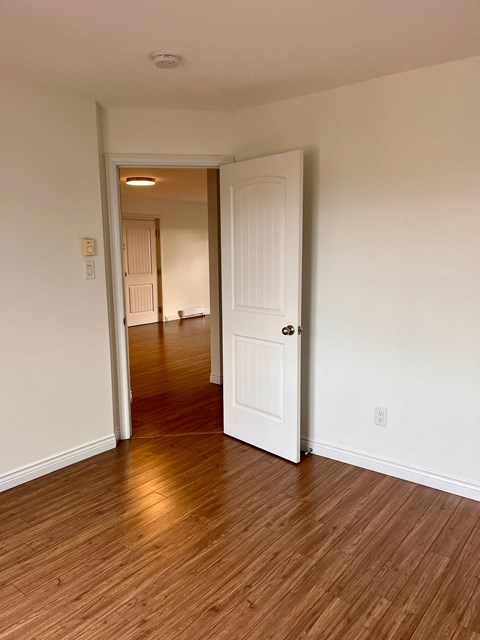 A hallway with a white door and wooden floors.