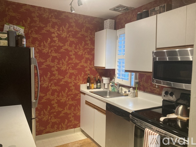 A kitchen with a black fridge, white cabinets, and a black stove top oven.
