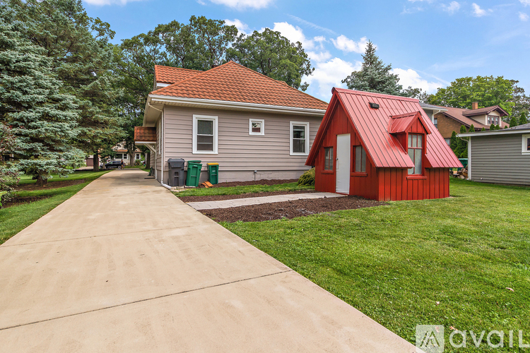 A house with a red roof is situated in a grassy area with a concrete pathway leading to it.