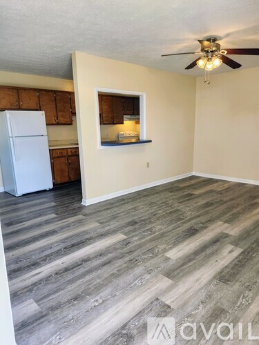 A room with a white fridge and wooden flooring.