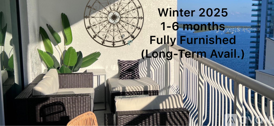 A room with a view of the sea, featuring a sofa, a chair, and a plant, with a decorative wall hanging and a dartboard.