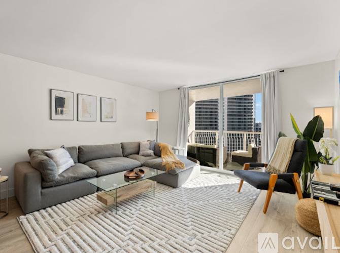 A living room with a grey sofa, a glass coffee table, and a large window with a view of the city.
