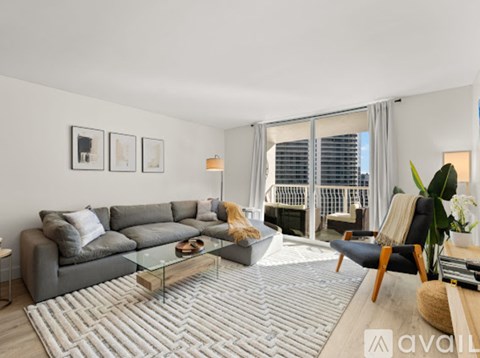 A living room with a grey sofa, a glass coffee table, and a large window with a view of the city.