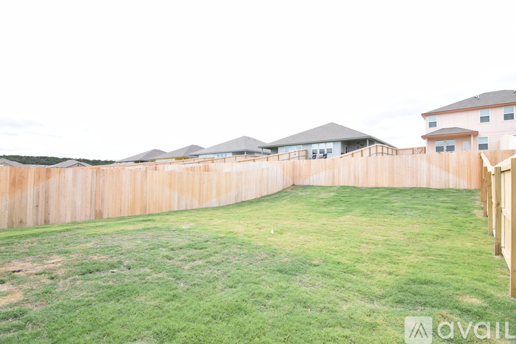 A grassy yard with a wooden fence and houses in the background.
