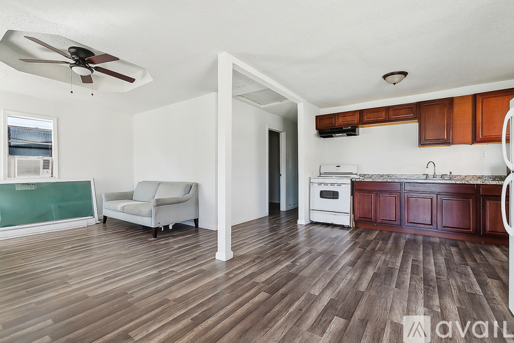 A living room with a couch, a fan, and a kitchen area with wooden floors.