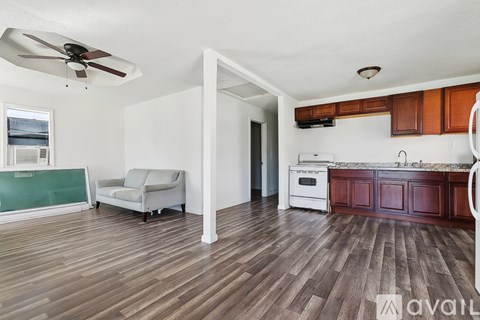 A living room with a couch, a fan, and a kitchen area with wooden floors.