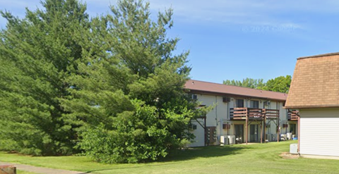 A white building with a brown roof is surrounded by green trees.