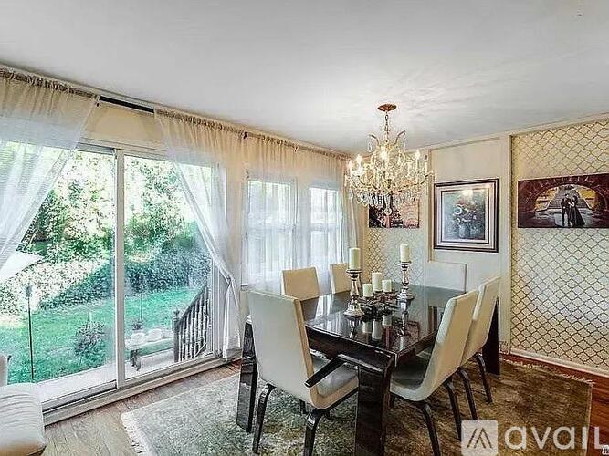 A dining room with a glass table and chairs, a chandelier, and a view of the backyard through the sliding glass doors.