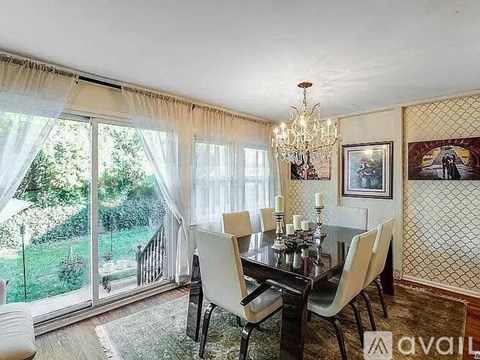 A dining room with a glass table and chairs, a chandelier, and a view of the backyard through the sliding glass doors.