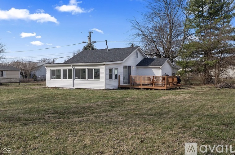 A house with a white exterior and a brown deck is surrounded by a grassy field.