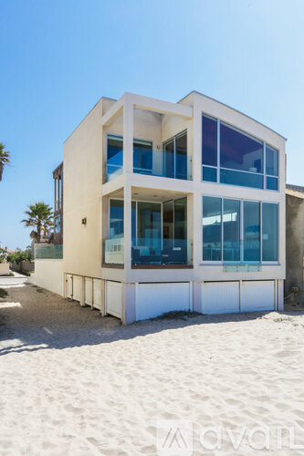 A modern house with a flat roof and large windows is situated on a sandy beach.
