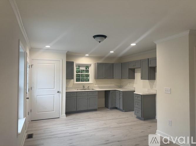 A spacious kitchen with grey cabinets and a white door.