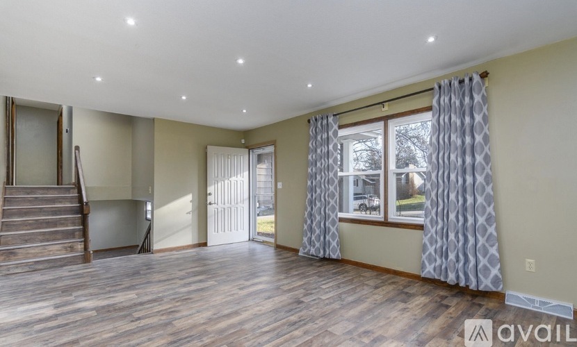 A spacious room with wooden floors and a staircase leading to another level.