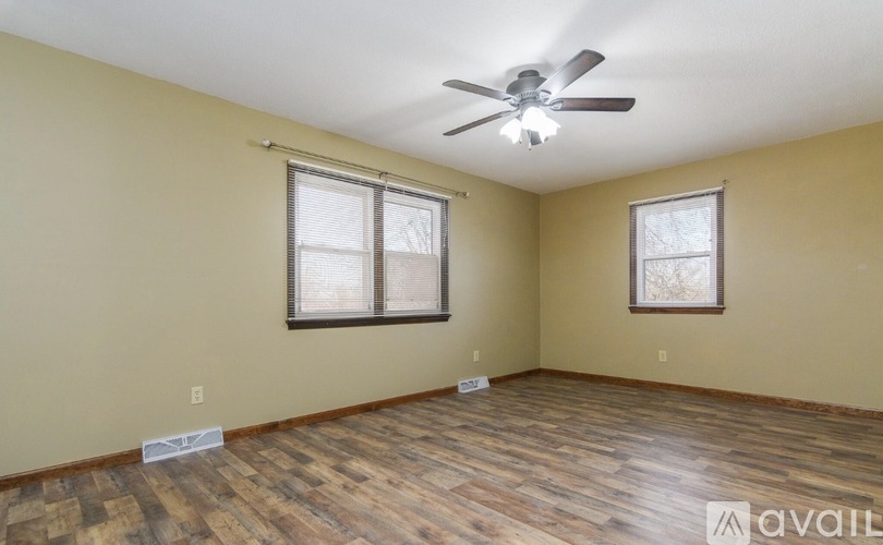 A room with a ceiling fan and two windows.