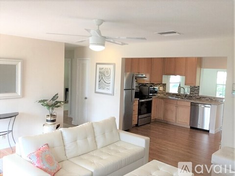A living room with a white couch and a kitchen in the background.