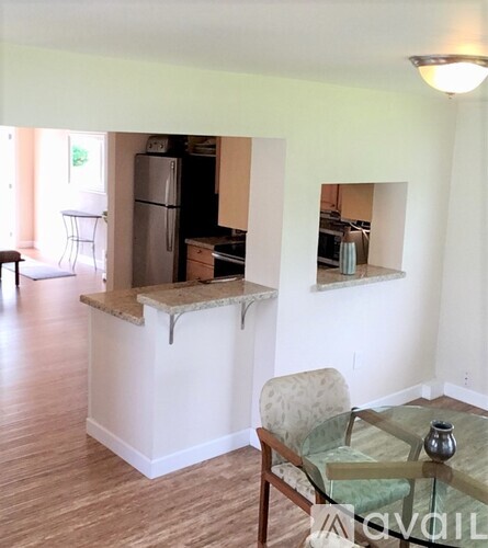 A kitchen with a refrigerator, a table with a vase, and a chair.