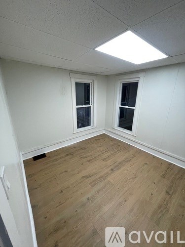 A room with wooden flooring and two windows.