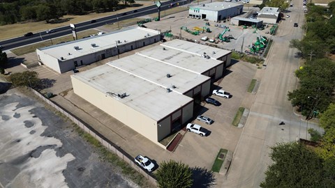 An aerial view of a large industrial building with a parking lot in front.