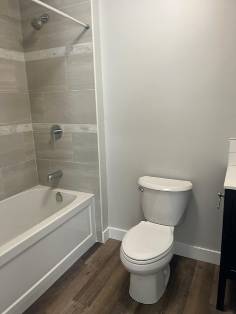 A white toilet in a bathroom with a white tub and tiled walls.