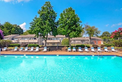 A swimming pool surrounded by lawn chairs and trees.