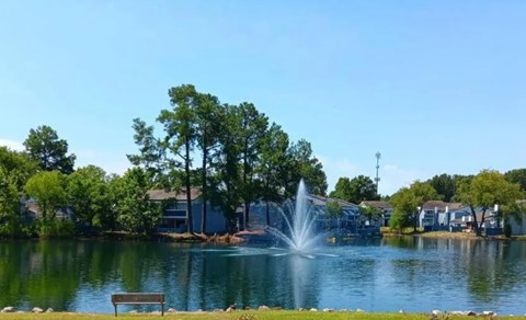 A fountain in the middle of a lake surrounded by trees and houses.