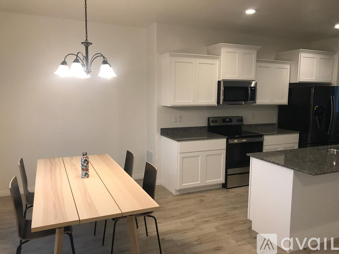 A kitchen with a table and chairs in the foreground and a black refrigerator in the background.