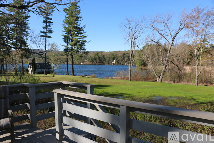 A wooden deck overlooks a lake with a house and trees in the distance.