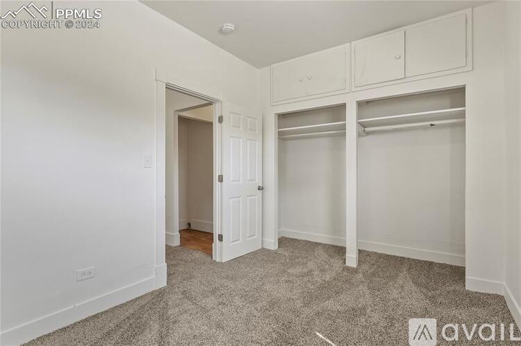 A room with white walls and a carpeted floor with a doorway leading to another room.