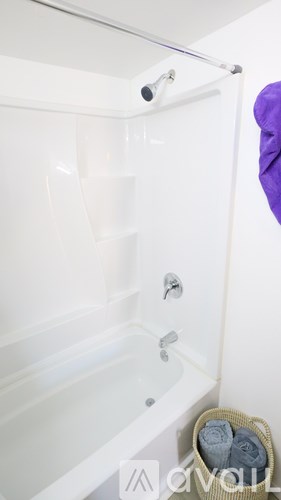 A white bathtub with a shower head and a basket of towels.
