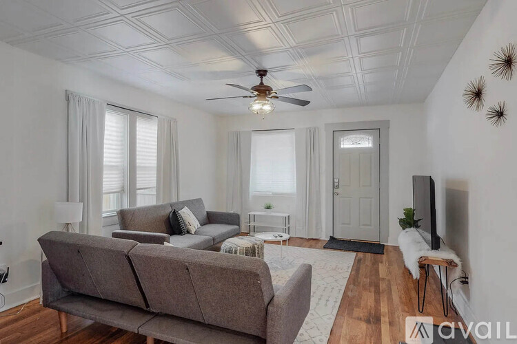 A living room with a grey couch, a ceiling fan, and a television.