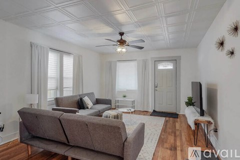 A living room with a grey couch, a ceiling fan, and a television.
