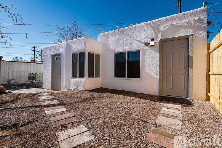 A white house with a brown door and windows is surrounded by a gravel driveway.