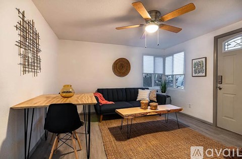 A living room with a black couch, a wooden table, and a ceiling fan.