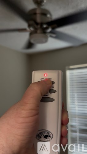 A hand is holding a remote control with a red dot on it.