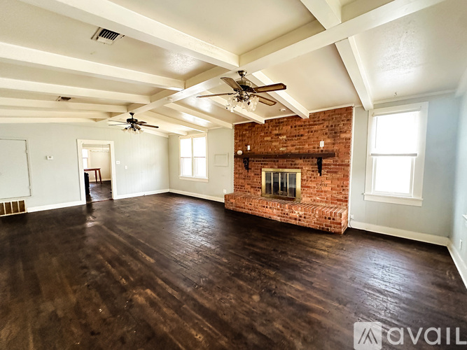 A spacious room with a brick fireplace and wooden floors.